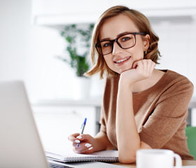 Mujer trabajando sonriendo mientras apunta en un libreta